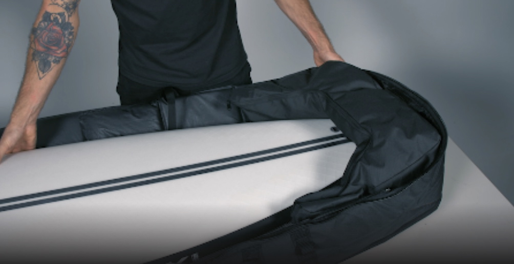 Mann schiebt ein weißes Surfboard im Studio in eine schwarze gepolsterte Boardbag