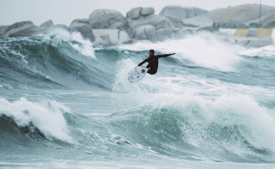 Surfer im Winter-Neoprenanzug mit Kopfhaube geht ins kalte Wasser