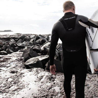 Surfer im Neoprenanzug zieht am Meer einen Handschuh an