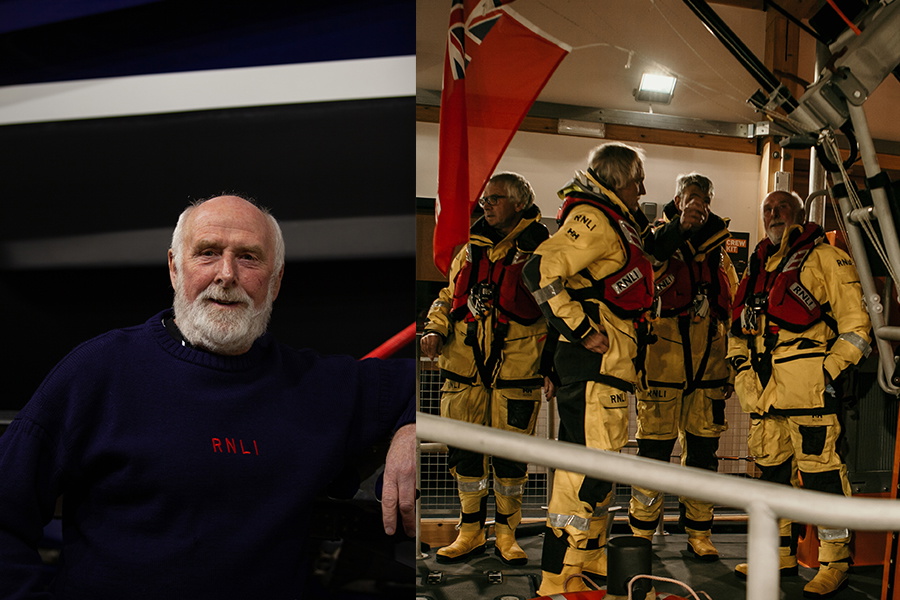 Bearded RNLI volunteer portrait alongside crew in yellow kit gathered in a lifeboat station