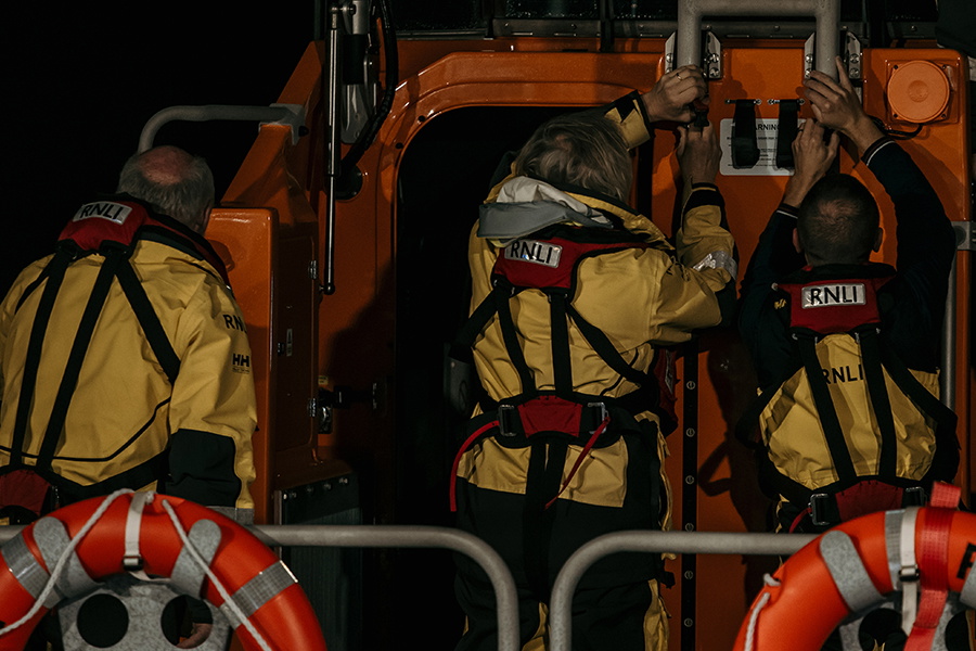 Lifeboat crew in yellow drysuits and lifejackets standing aboard an orange RNLI lifeboat