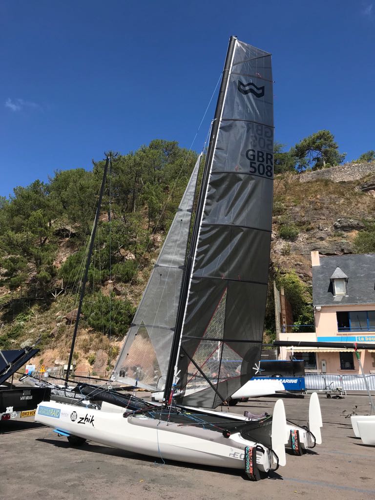 Formula 18 racing catamaran with a grey mainsail rigged on the slipway below a wooded hillside