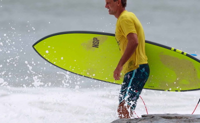 Mann läuft mit einem Surfboard ins Meer